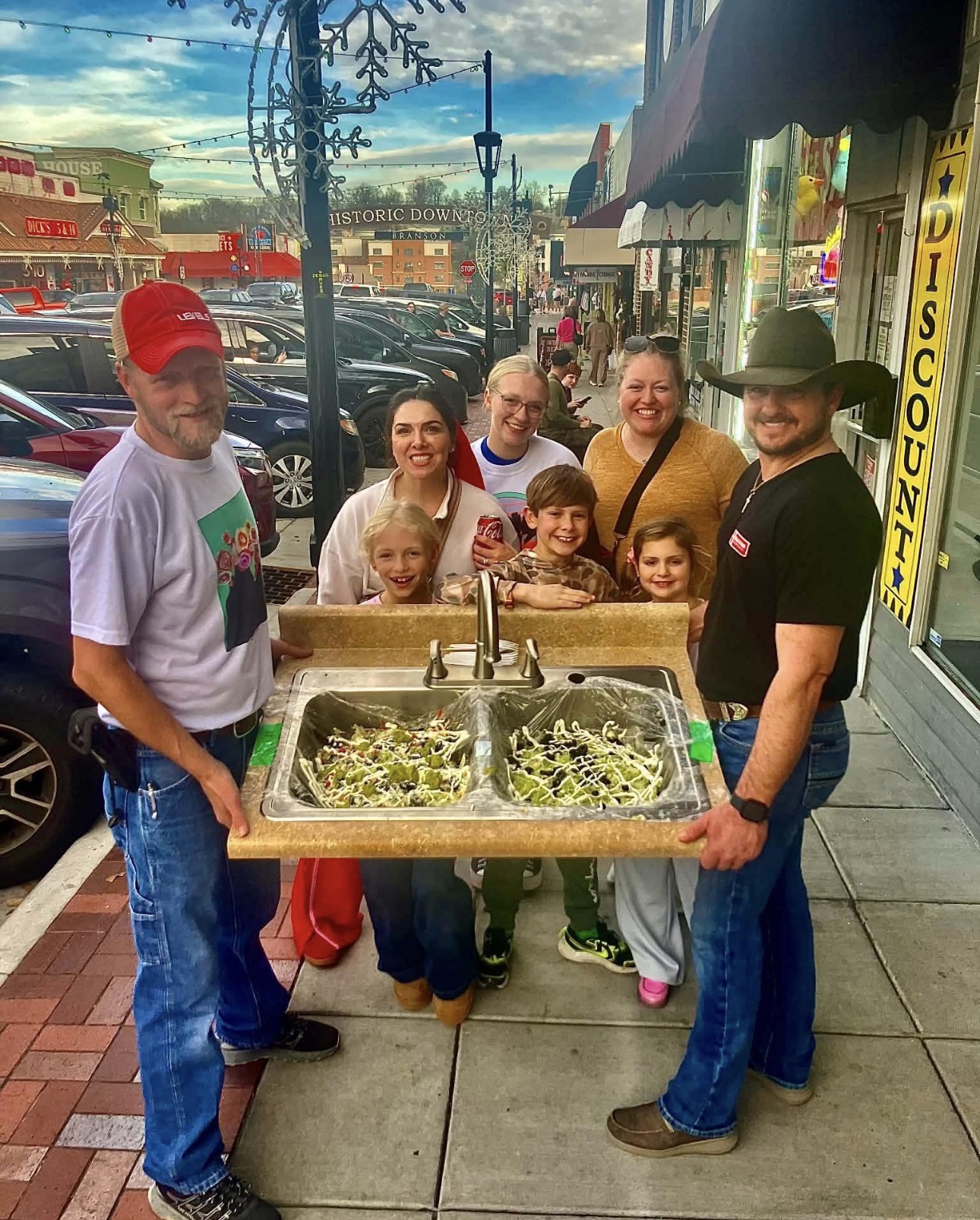 Family on Branson's Historic Downtown holding a double kitchen sink loaded with two giant walking tacos at Walkers